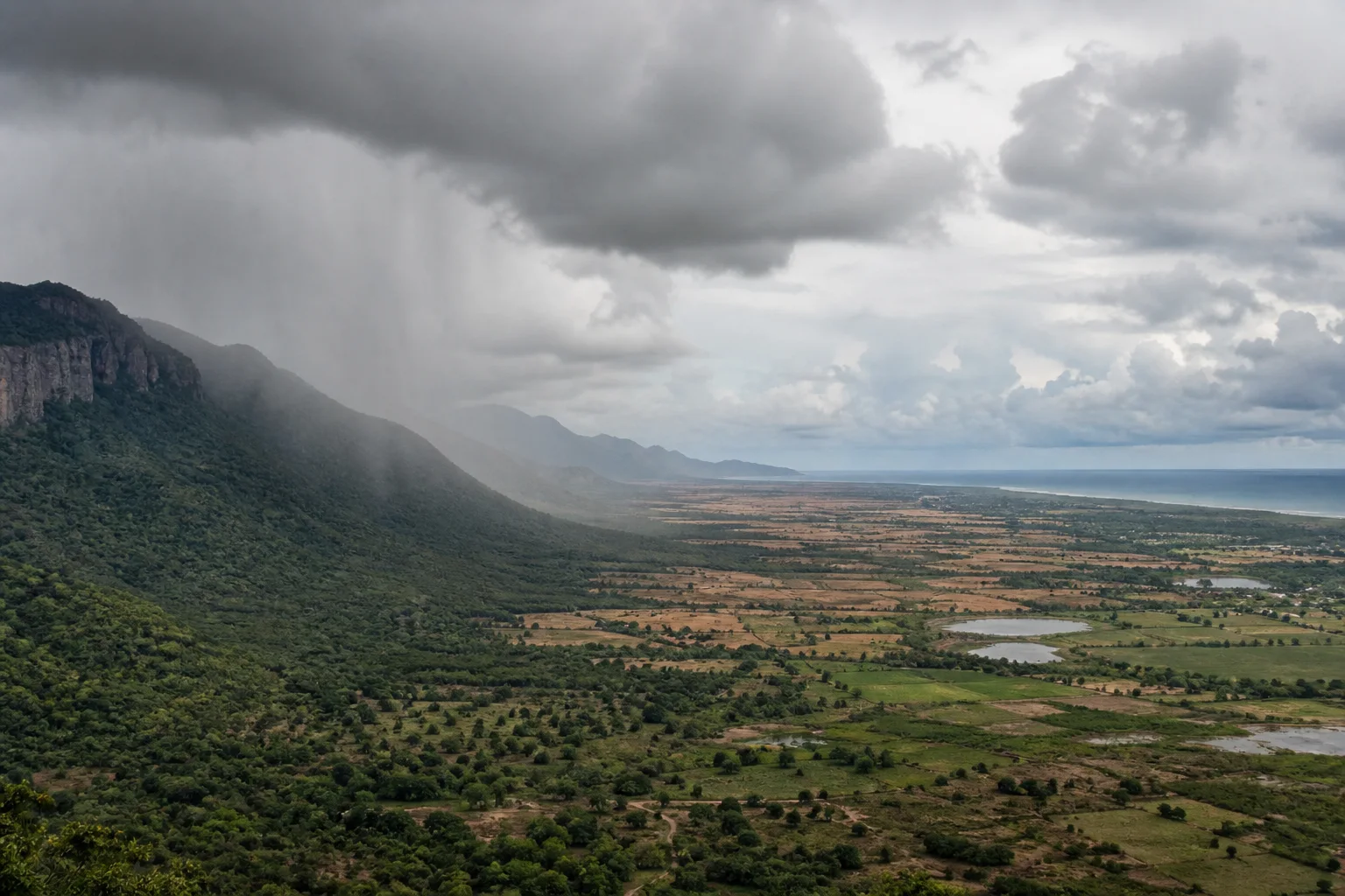 Editorial landscape interpretation showing rain over a western mountain edge, a drier interior plain and clouds toward the Tamil Nadu coast